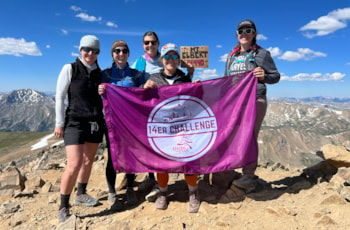 Solemates participants in the 14er Challenge smiling with a GOTR flag at the summit